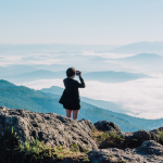 Una mujer mira las vistas en la cima de un monte con su ropa Salomon. (Fuente: Canva) ella-hoy.es