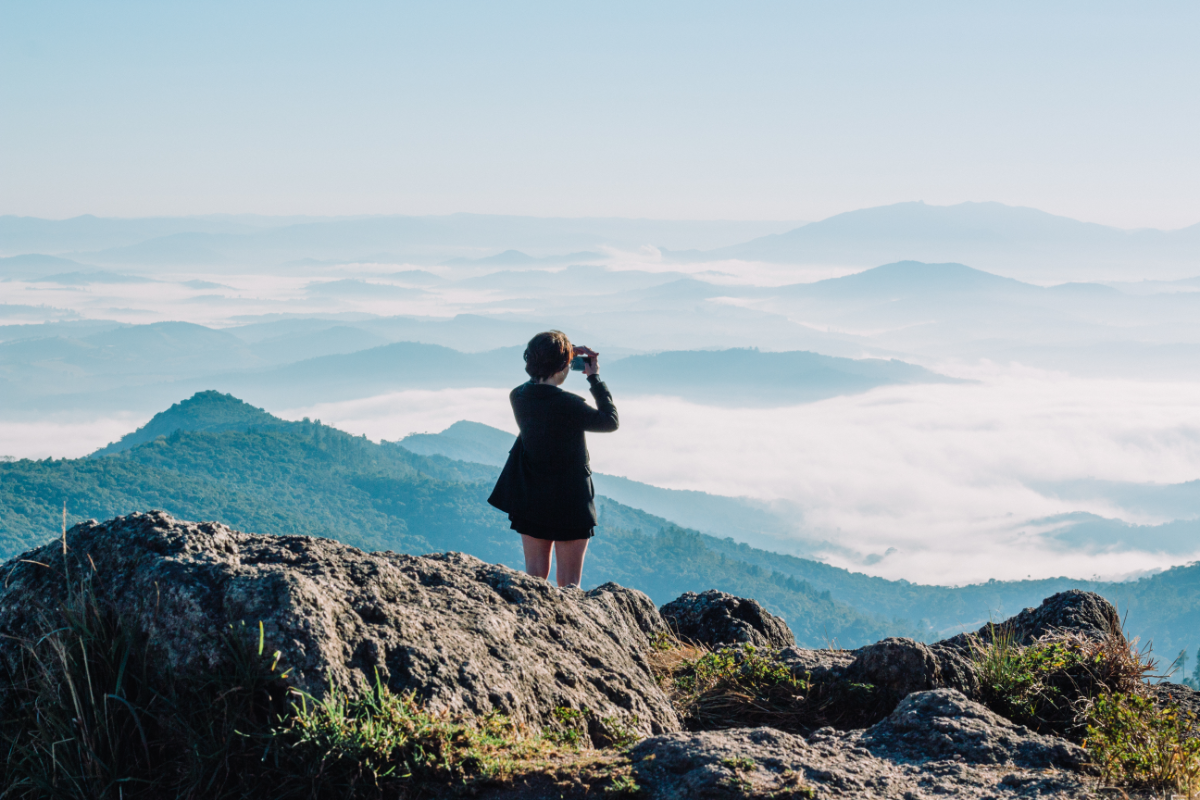 Una mujer mira las vistas en la cima de un monte con su ropa Salomon. (Fuente: Canva)ella-hoy.es
